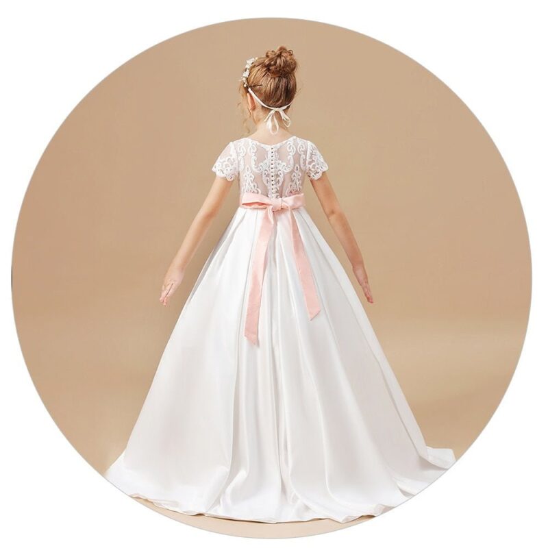 Back view of an ivory satin flower girl dress with lace illusion back, blush pink bow sash and elegant full length skirt