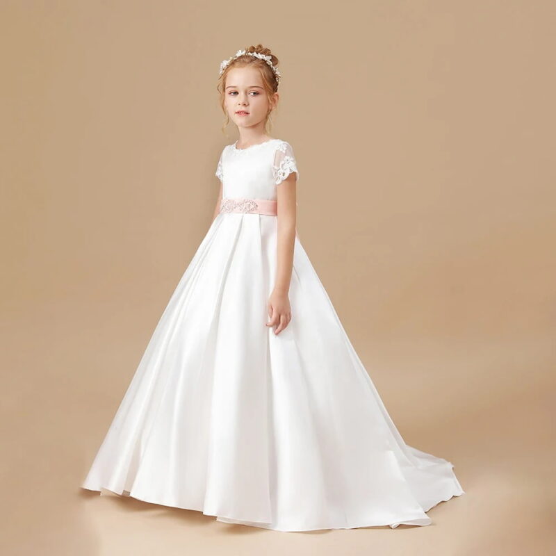 Side view of an ivory satin flower girl dress with lace sleeves, blush pink embellished sash and elegant full length skirt
