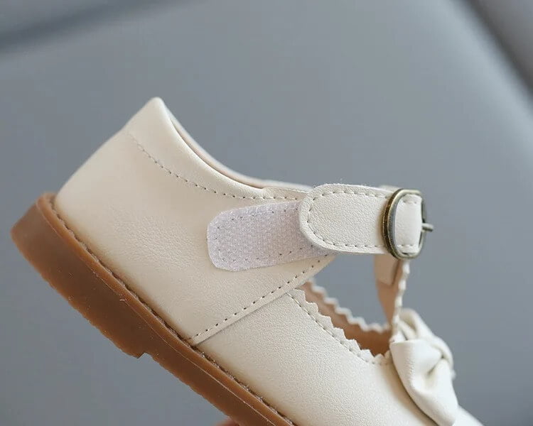 Close-up side view of girls off white T-bar bow shoes showing adjustable hook and loop fastening, velcro, and durable sole