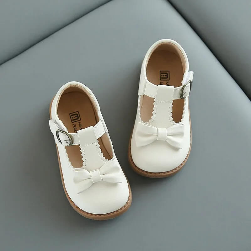 Pair of girls off white T-bar shoes with bow detail, buckle fastening and classic formal shoe styling for special occasions
