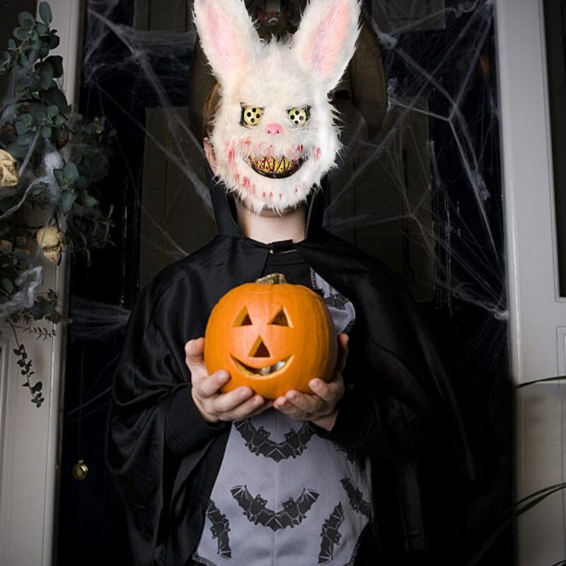 Person wearing a horror rabbit mask holding a carved pumpkin during Halloween