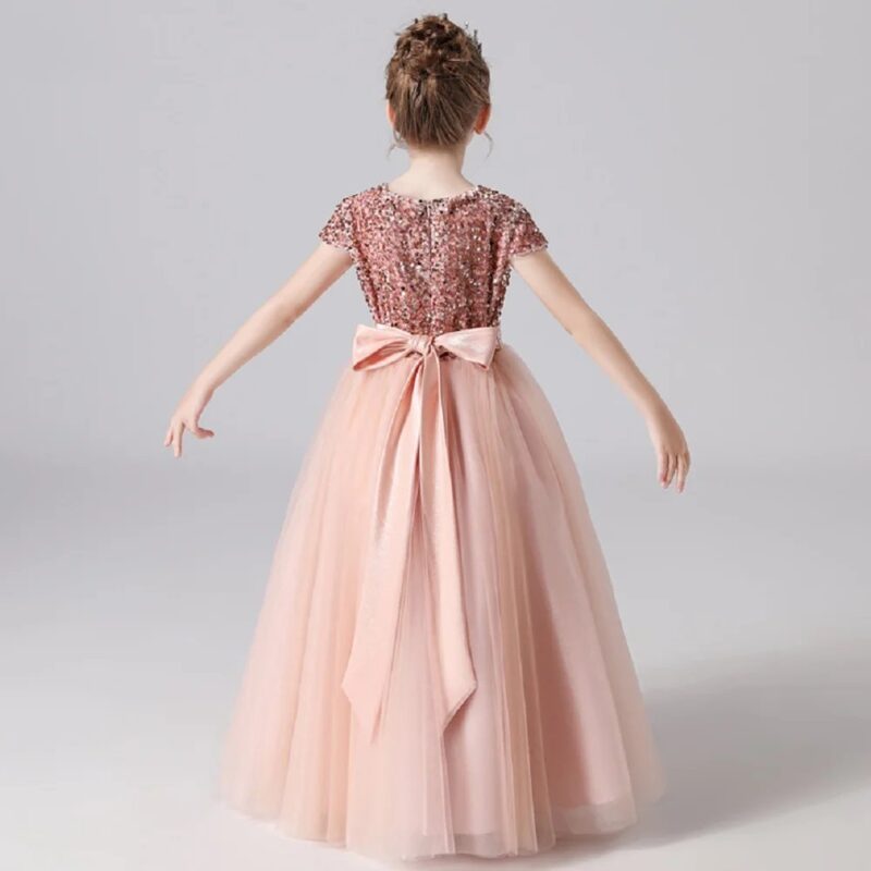 Back view of pink sequin flower girl gown featuring large satin bow and flowing layered tulle skirt for formal occasions.