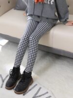 Girl wearing black and white houndstooth winter leggings while seated, styled with a grey sweatshirt and black boots.