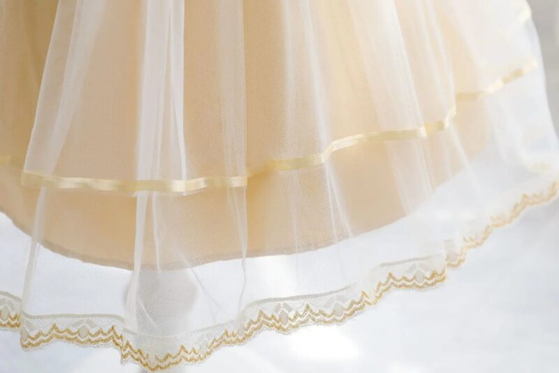 Close-up of champagne flower girl dress layered tulle skirt with satin ribbon and gold embroidered lace hem