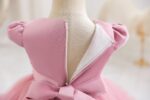 Back detail of dark pink girls occasion dress showing concealed zip fastening, puff sleeves and large waist bow
