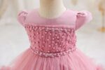 Close-up of dark pink girls occasion dress with puff sleeves, pearl embellished bodice and floral trim