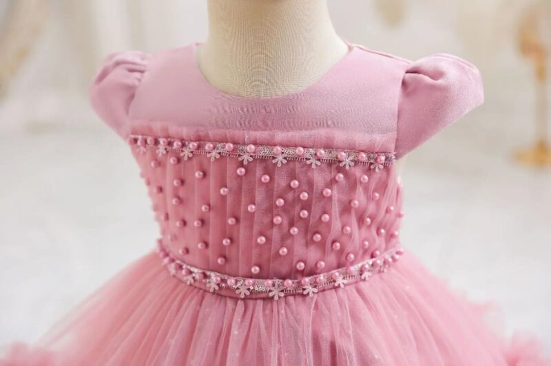 Close-up of dark pink girls occasion dress with puff sleeves, pearl embellished bodice and floral trim