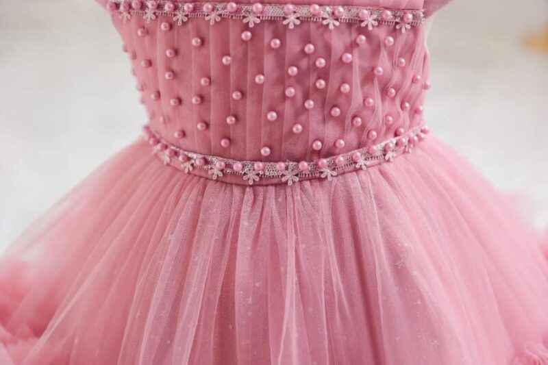 Close-up of pearl embellished dark pink bodice and decorative floral trim on girls tulle occasion dress