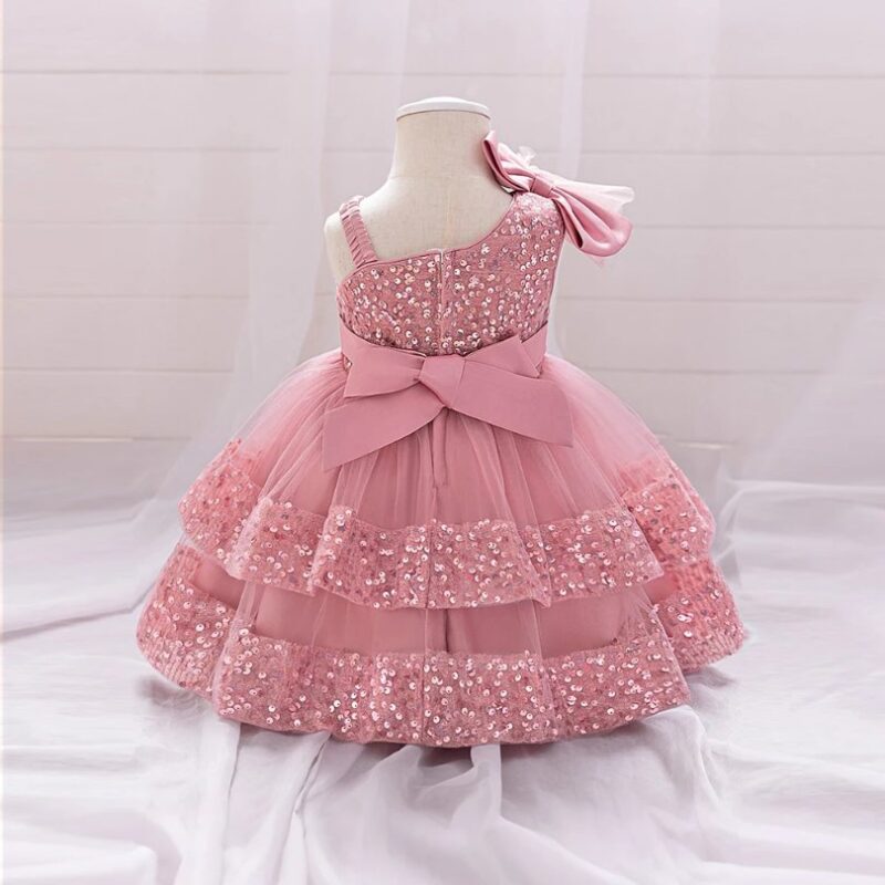 Back view of pink one shoulder sequin tulle gown for toddler girls with large bow and layered skirt