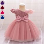 Pink baby party dress with asymmetric sequin bodice, flutter sleeve, large waist bow and full layered tulle skirt.