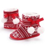 Pair of Baby Fair Isle Pom Pom Christmas booties with knitted snowflake pattern, ribbon bows and fluffy pom poms