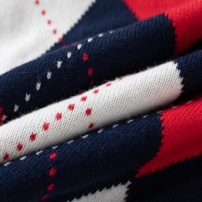 Close-up of soft knitted fabric on kids argyle jumper showing navy, red and white diamond pattern and fine stitch detail.