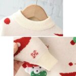 Close-up of cream kids Christmas jumper showing the ribbed crew neck, knitted fabric, red pattern and sleeve cuff detail.