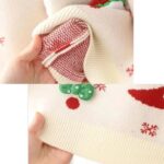 Close-up of cream kids Christmas jumper showing the knitted fabric construction, ribbed hem and festive chenille patch detail.