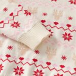 Close-up of kids cream Christmas jumper showing ribbed sleeve cuff with red snowflakes, reindeer and pink Fair Isle pattern.