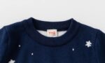 Close-up of kids polar bear Christmas jumper showing navy ribbed crew neck, snowflakes and soft knitted fabric.