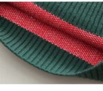 Close-up of inside hem on kids red Christmas jumper showing dark green ribbed trim and knitted fabric construction.
