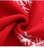 Close-up of soft red knitted fabric on kids Christmas reindeer jumper showing the material texture and white snowflake pattern.