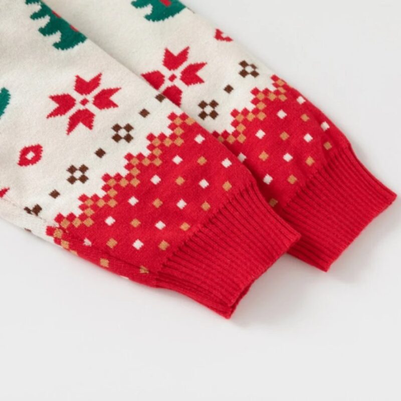 Close-up of kids cream Christmas jumper showing red ribbed sleeve cuffs, snowflakes and festive Fair Isle knitted pattern.