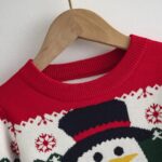 Kids Snowman Christmas Jumper (3) Close-up of kids snowman Christmas jumper showing the red ribbed crew neck, snowflake pattern and black snowman hat.